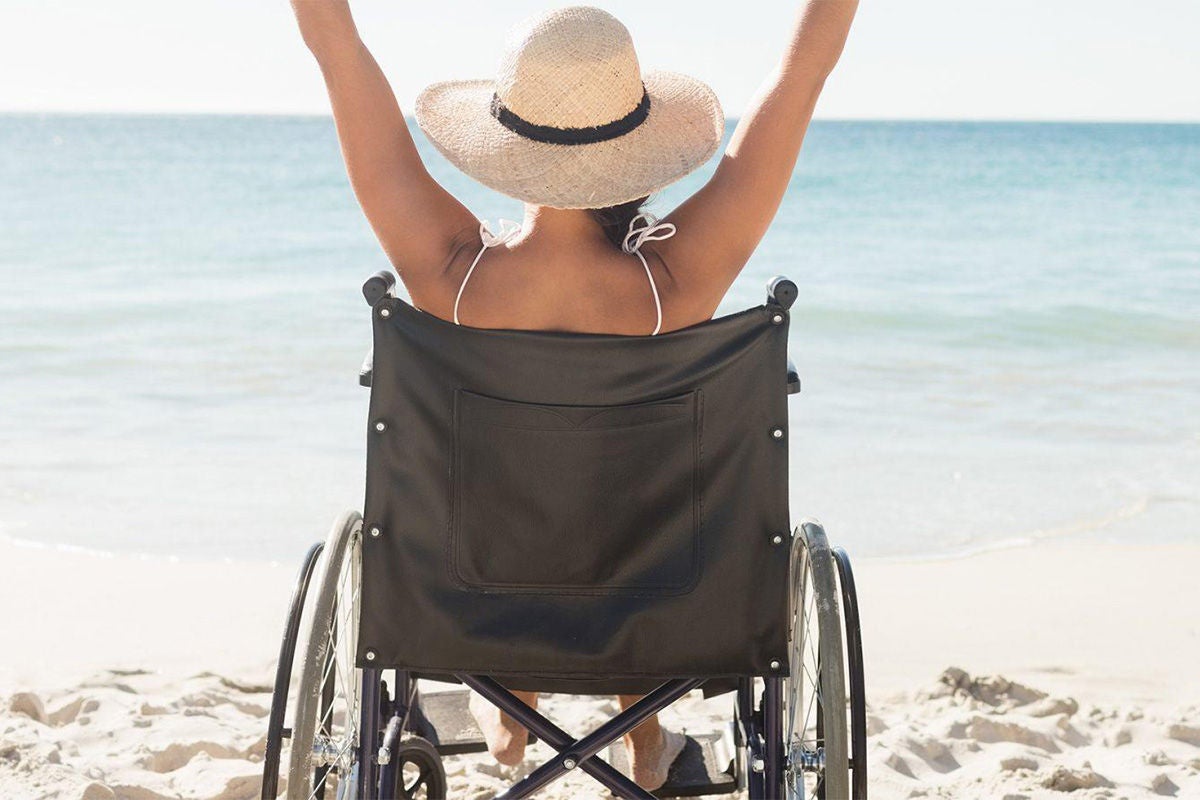 A woman in a wheelchair is on the beach looking at the water. 